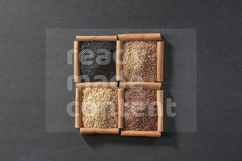 4 مربعات من عيدان القرفة ممتلئة بحبة البركة السوداء وبذور السمسم وبذور الكتان وحبوب الخردل على أرضية سوداء