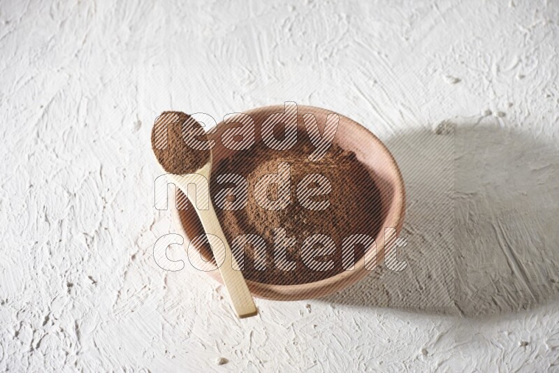 A wooden bowl and a wooden spoon full of cloves powder on a textured white flooring