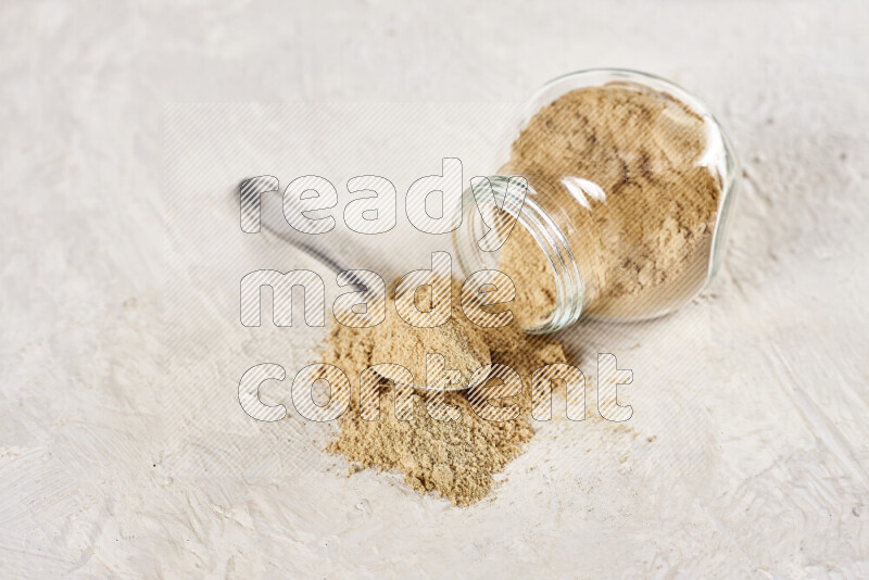A glass jar full of ground ginger powder flipped with some spilling powder on white background