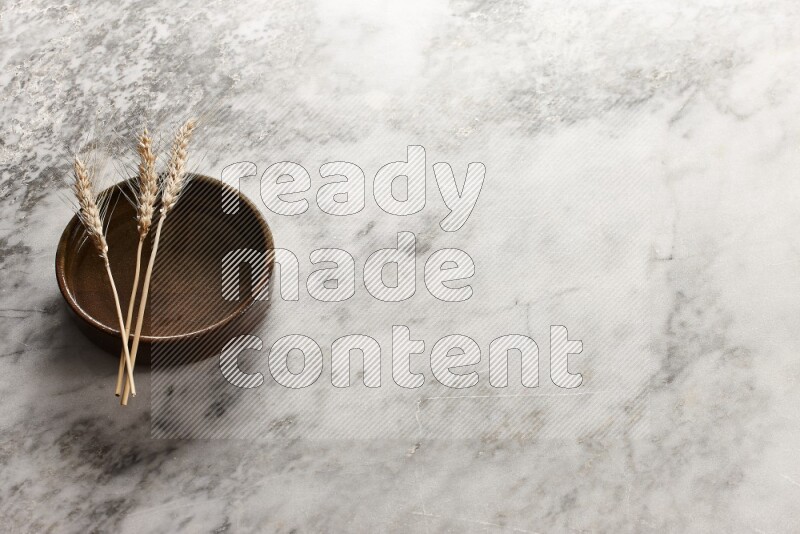 Wheat stalks on multicolored pottery oven plate on grey marble background