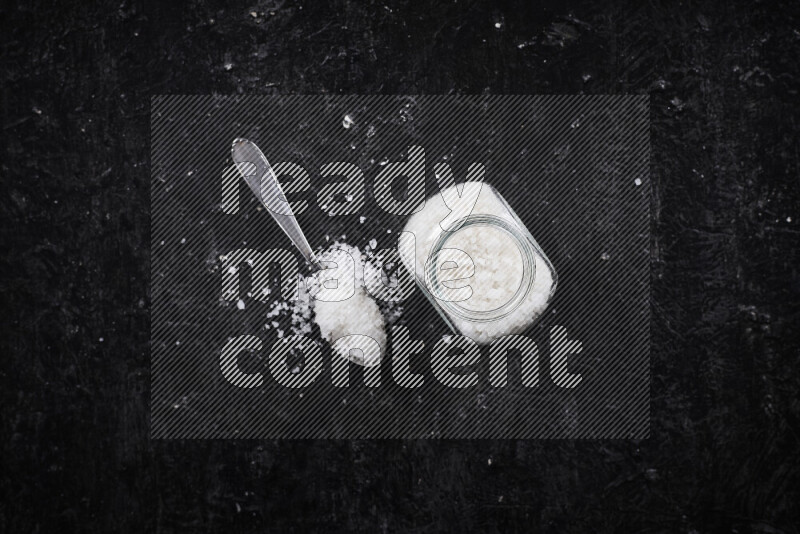 A glass jar full of coarse sea salt crystals on black background
