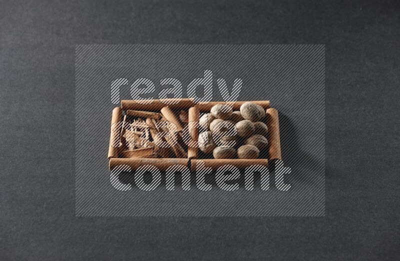 مربعان من أعواد القرفة ممتلئان بقطع من القرفة وجوزة الطيب علي خلفية سوداء