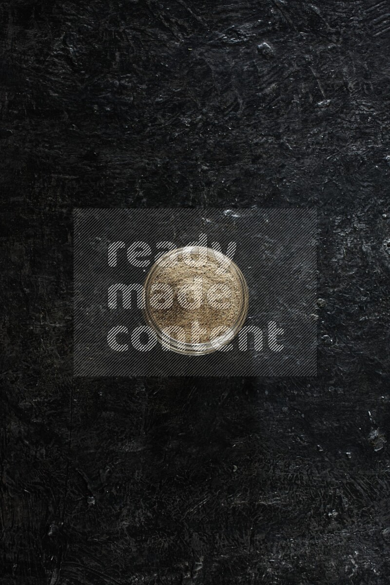 وعاء زجاجي ممتلئ ببودرة الهيل على خلفية سوداء