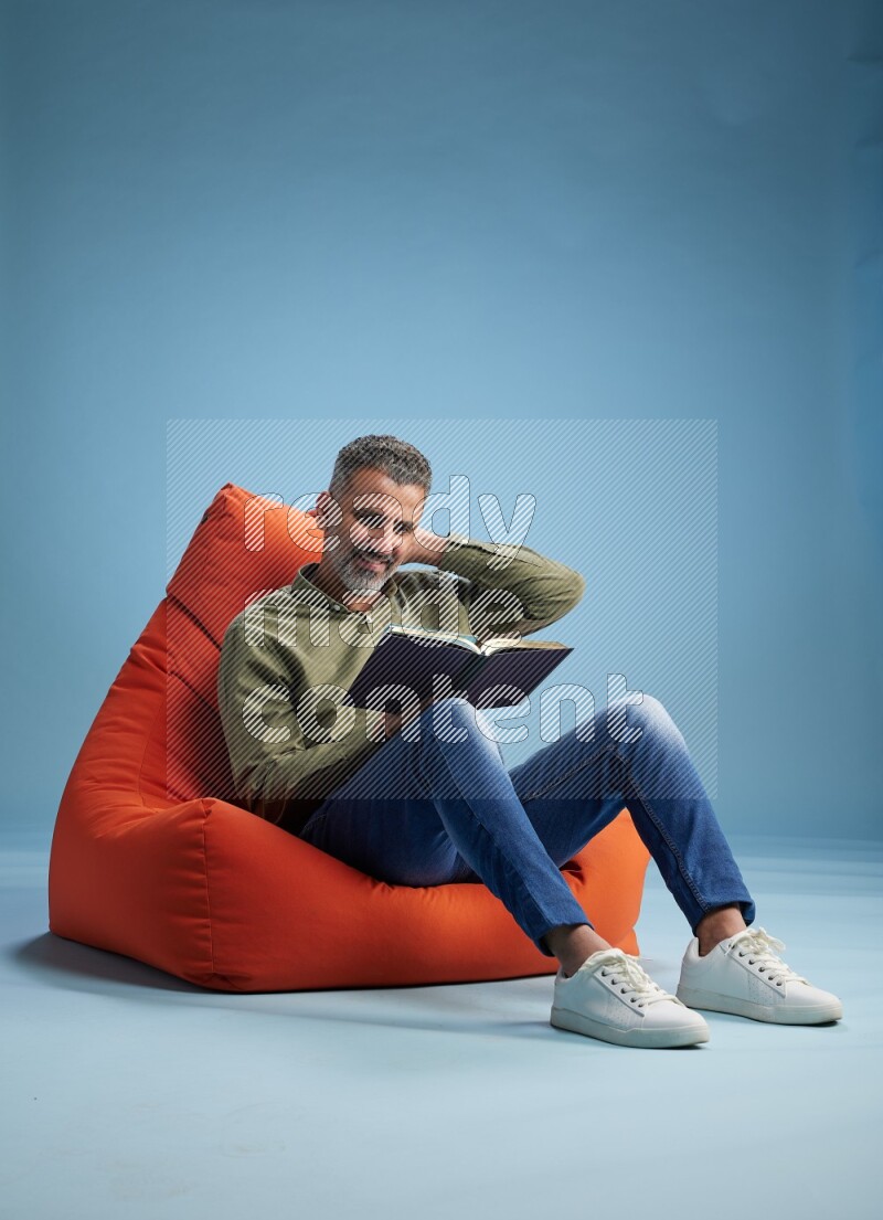 A man sitting on an orange beanbag and reading a book