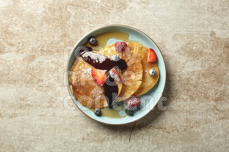 Three stacked mixed berries pancakes in a blue plate on beige background