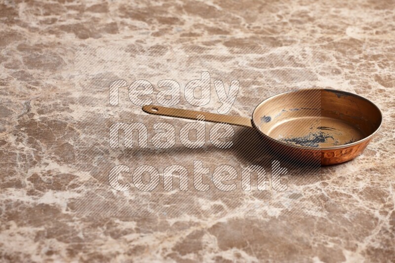 A small copper pan on beige marble background