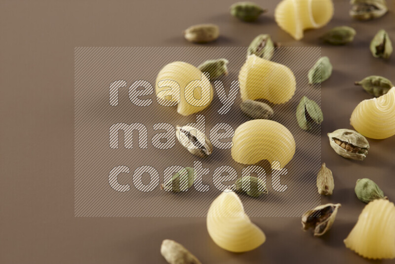 Raw pasta with different ingredients such as cherry tomatoes, garlic, onions, red chilis, black pepper, white pepper, bay laurel leaves, rosemary and cardamom on beige background