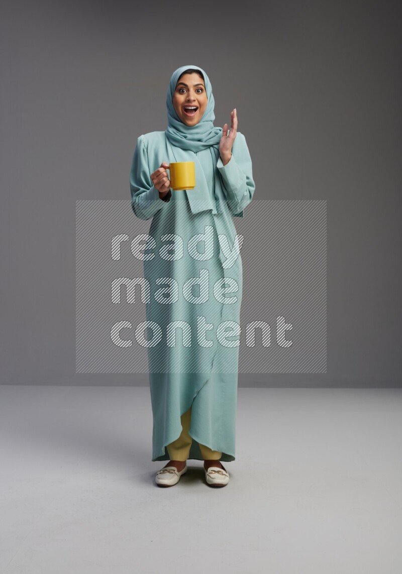Saudi Woman wearing Abaya standing  holding a mug on Gray background