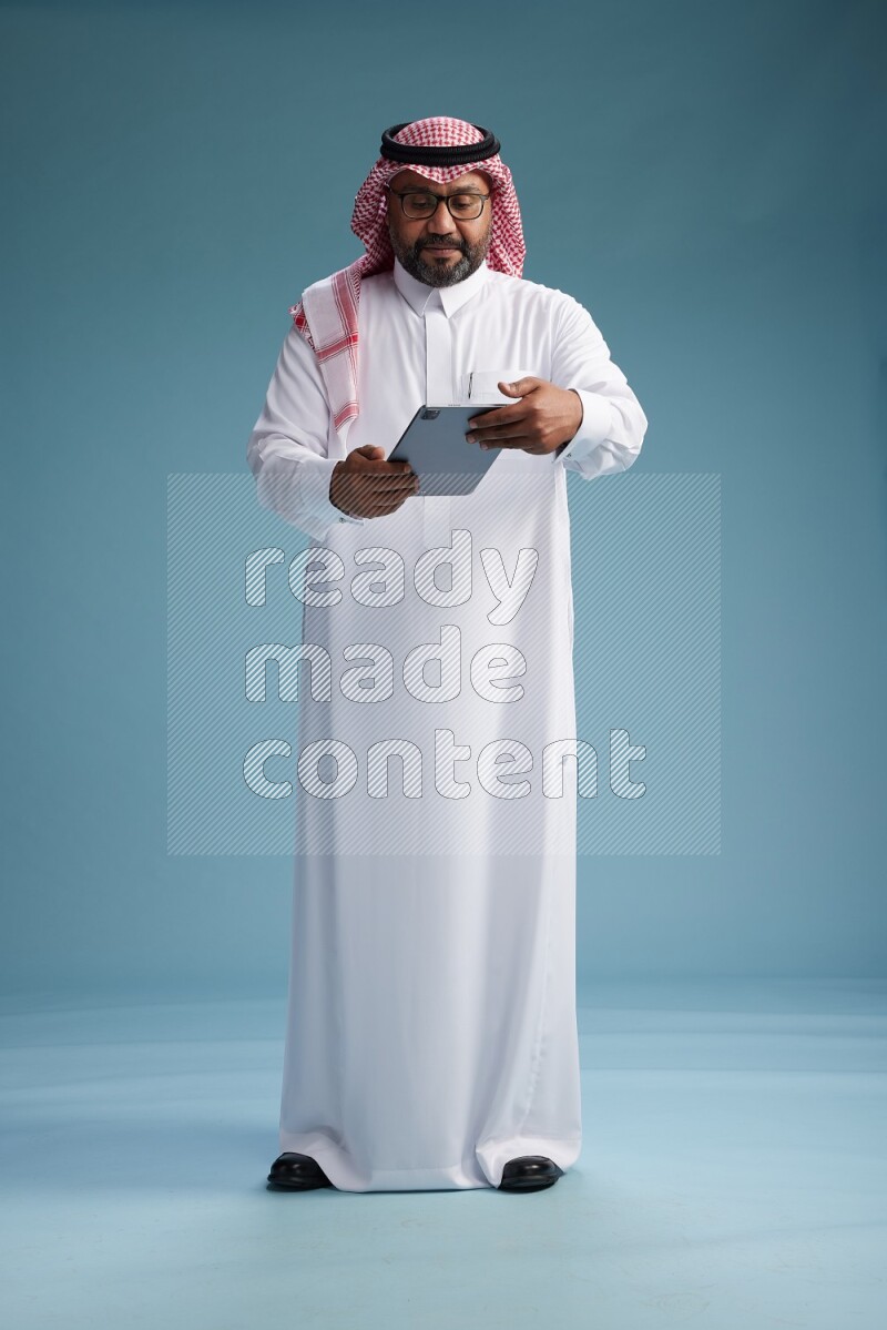 Saudi Man with shimag Standing holding a tablet on blue background