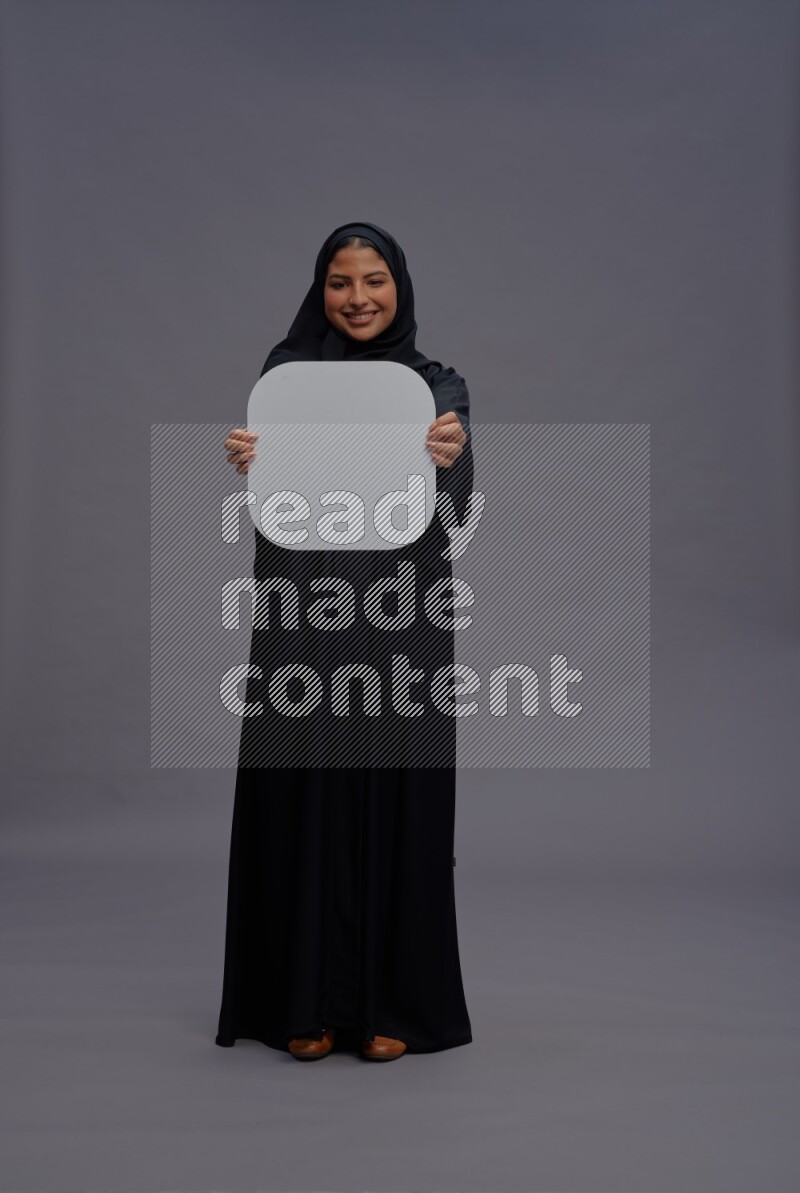 Saudi woman wearing Abaya standing holding social media sign on gray background