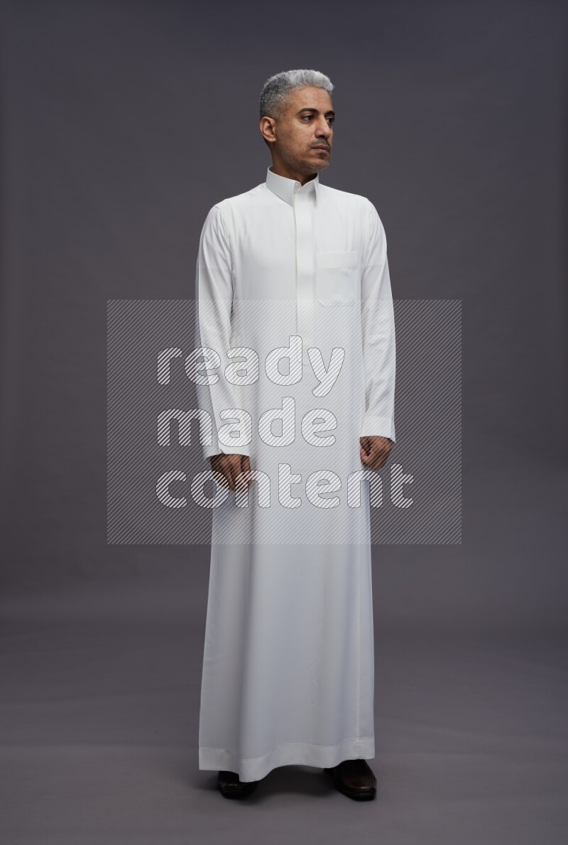 Saudi man wearing thob standing interacting with the camera on gray background