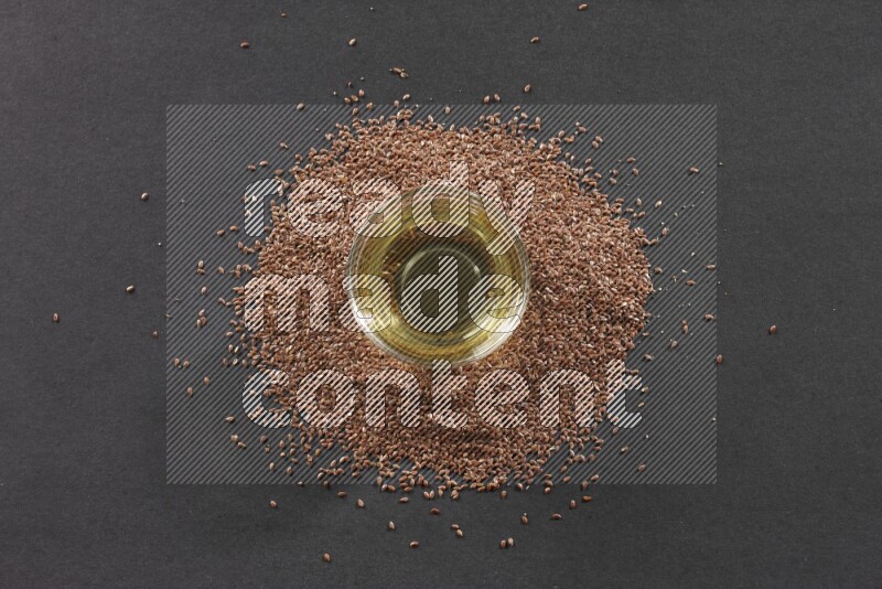 وعاء زجاجي ممتلئ بزيت بذر الكتان محاط بحبوب بذر الكتان علي خلفية سوداء