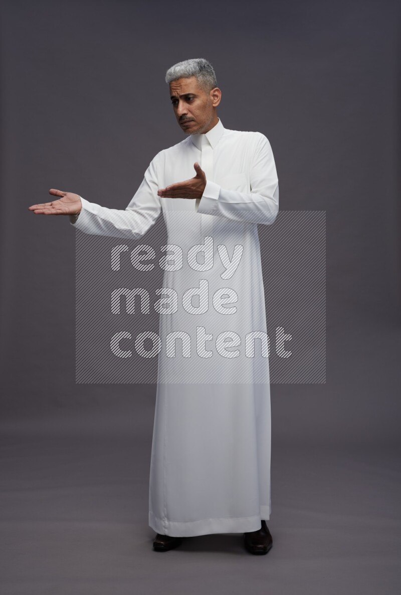 Saudi man wearing thob standing interacting with the camera on gray background