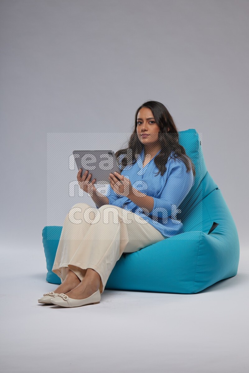 A woman sitting on a blue beanbag and working on tablet