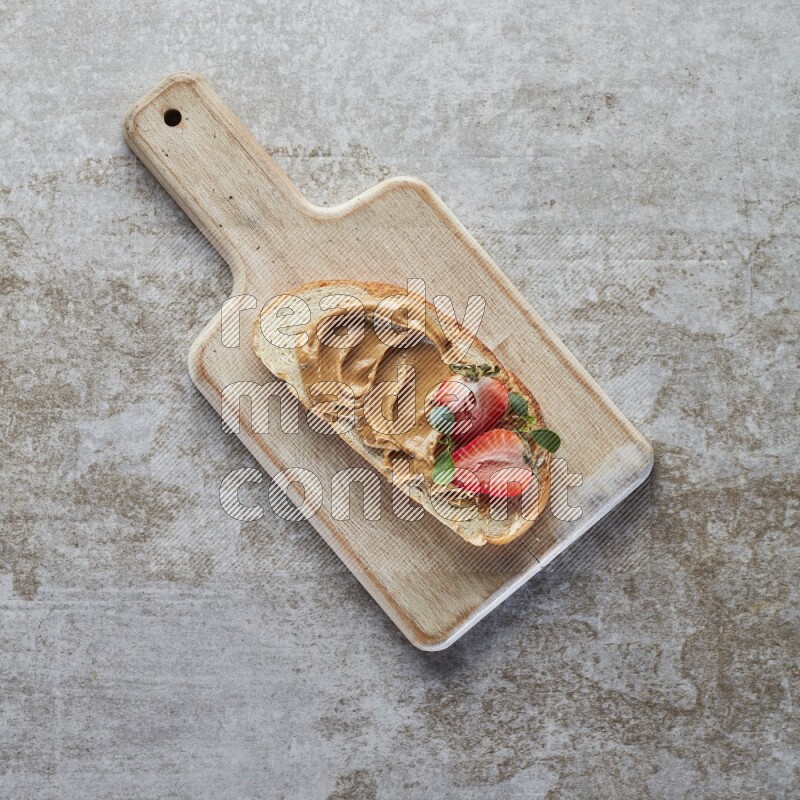 open faced peanut butter sandwich with strawberries on a grey textured background