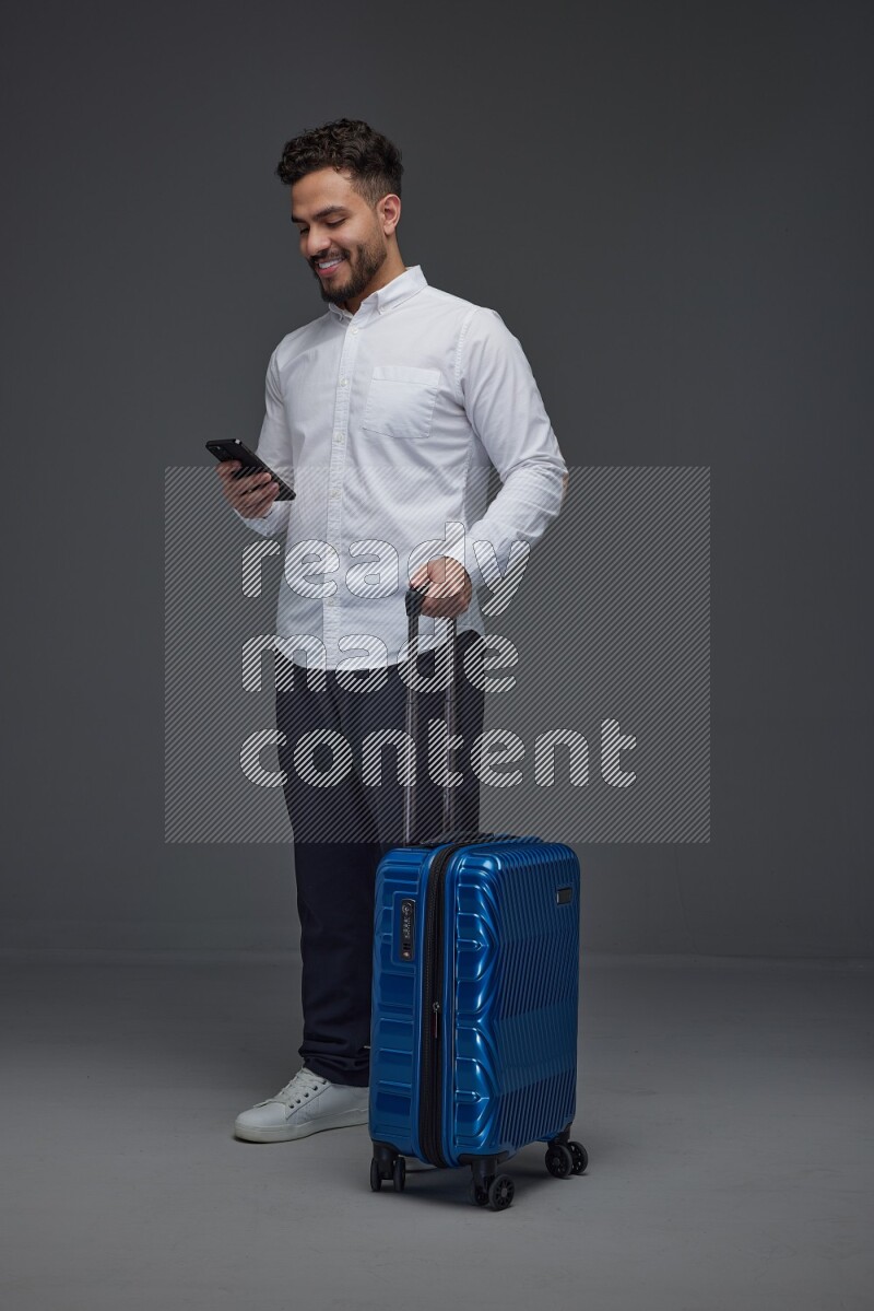 A man wearing smart casual holding luggage eye level on a gray background
