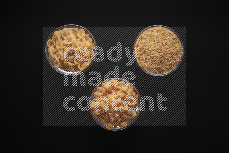 Different pasta types in glass bowls on black background