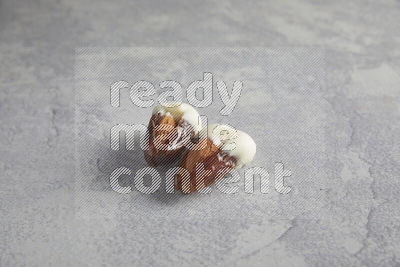 two almonds stuffed dates covered with white chololate on a light grey background