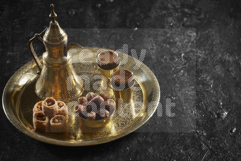 Oriental sweets with dates and a drink on a metal tray in a dark setup