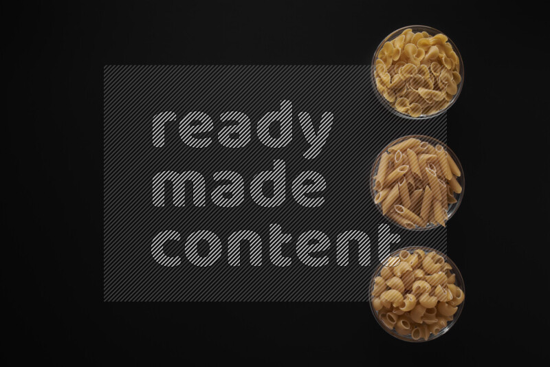 Different pasta types in 3 glass bowls on black background