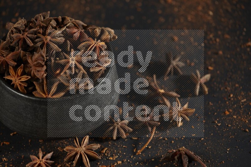 Star Anise in a black bowl with sprinkled anise on black flooring