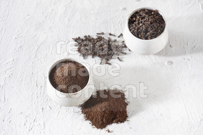 2 Beige ceramic bowls, one full of cloves and the other full of powder on textured white flooring