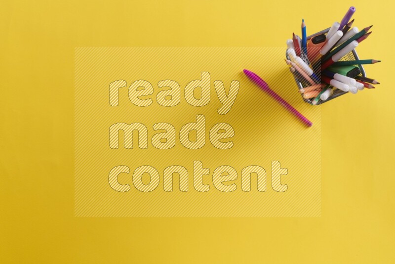 بعض الأقلام والمستلزمات المدرسية في مقلمة معدنية علي خلفية صفراء