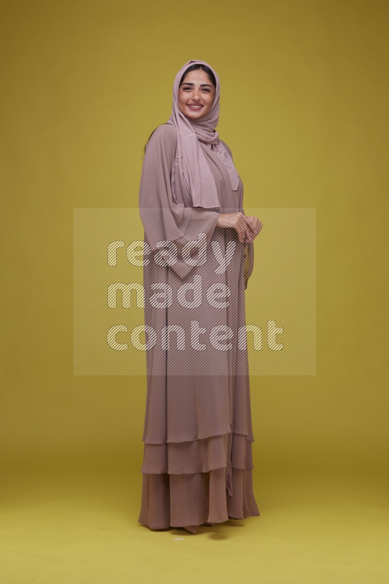A woman Posing on a Yellow Background wearing Brown Abaya with Hijab
