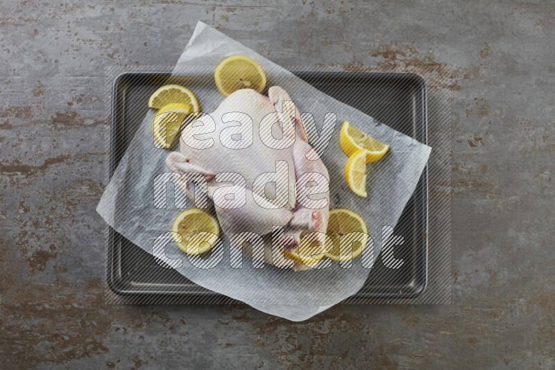 whole raw chicken on an oven trey direct on a rustic grey background