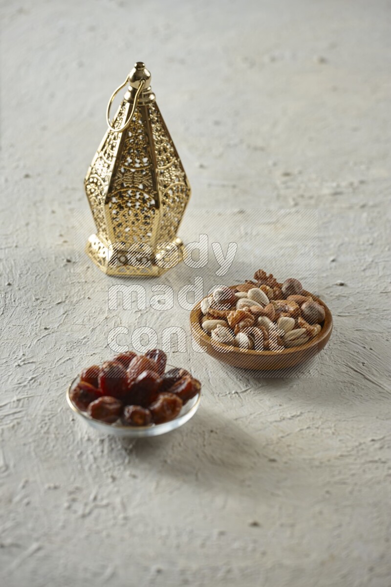 A golden lantern with different drinks, dates, nuts, prayer beads and quran on textured white background