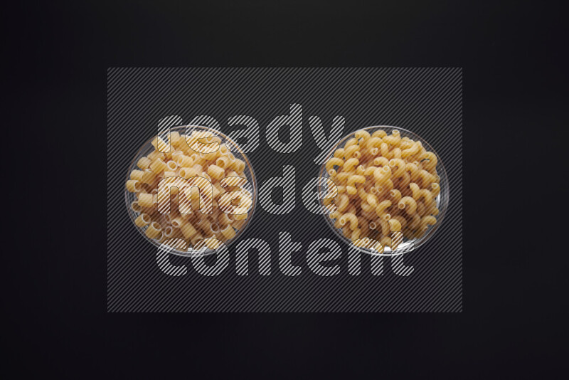 Different pasta types in glass bowls on black background
