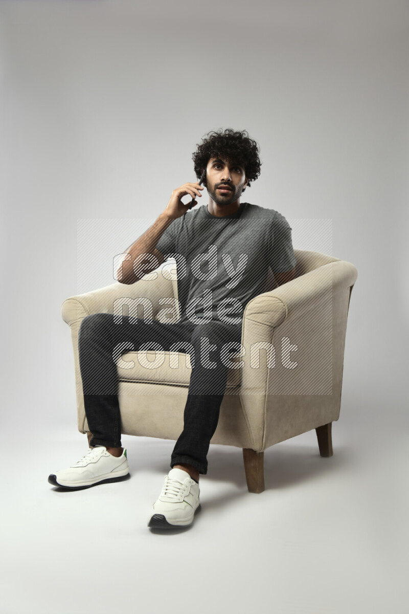A man wearing casual sitting on a chair talking on the phone on white background