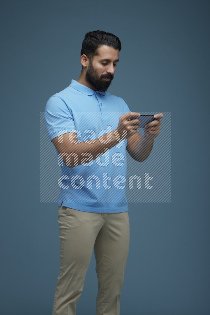 Man playing a game on his phone in a blue background wearing a Blue shirt