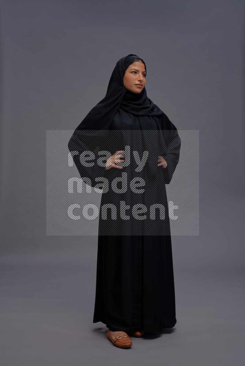 Saudi woman wearing Abaya standing interacting with the camera on gray background