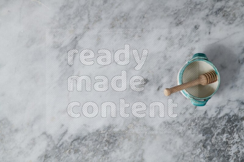 وعاء فخاري متعدد الألوان مع ملعقة عسل خشبية بداخله على خلفية من الرخام الرمادي