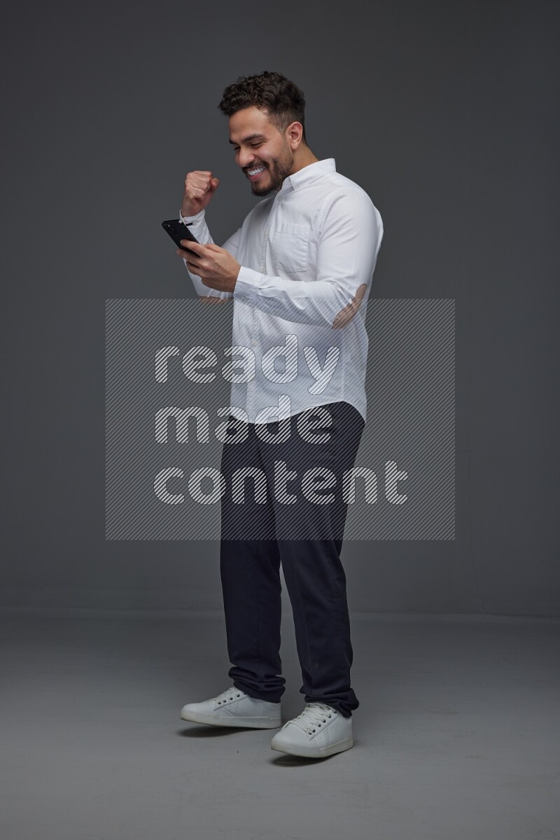 A man wearing smart casual standing and using his phone eye level on a gray background