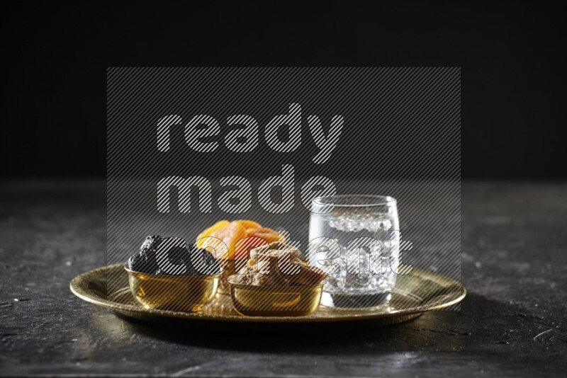 Dried fruits in metal bowls with water on a tray in dark setup