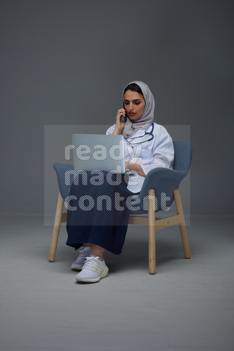A doctor wearing a light gray head scarf sitting on blue chair on grey background