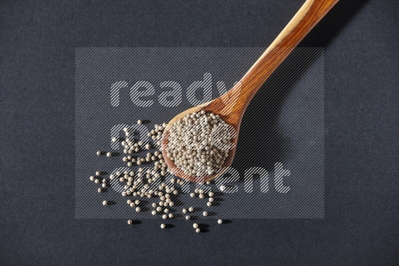A wooden ladle full of white pepper beads on black flooring