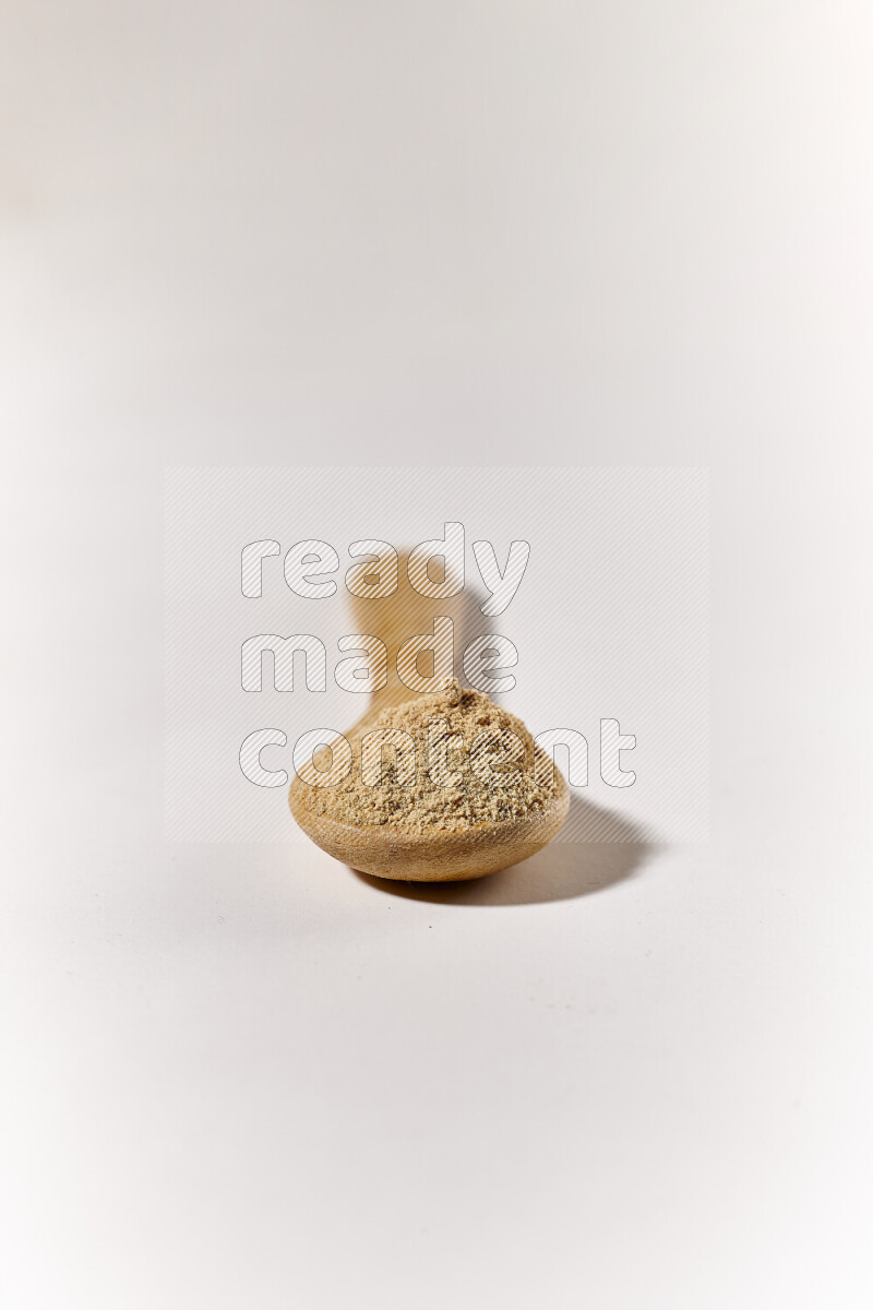 A wooden spoon full of ground ginger powder on white background