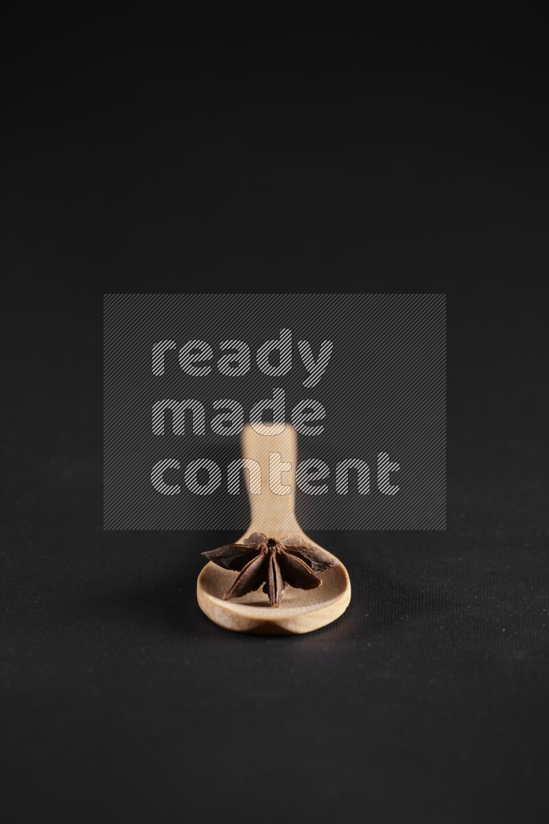 اليانسون النجمي في ملعقة خشبية فوق اليانسون النجمي الذي يغطي الإطار على أرضية سوداء