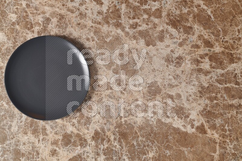 Top View Shot Of A Black Ceramic Circular Plate On beige Marble Flooring