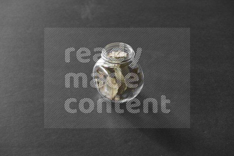 A glass spice jar full of bay laurel leaves on black flooring
