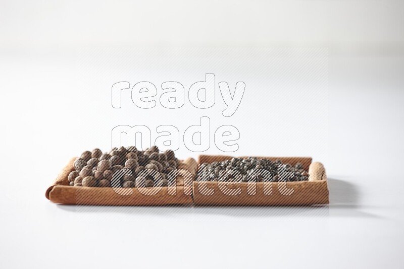 مربعان من أعواد القرفة ممتلئان بحبوب الفلفل الأسود وحبوب الفلفل الحلو علي خلفية بيضاء