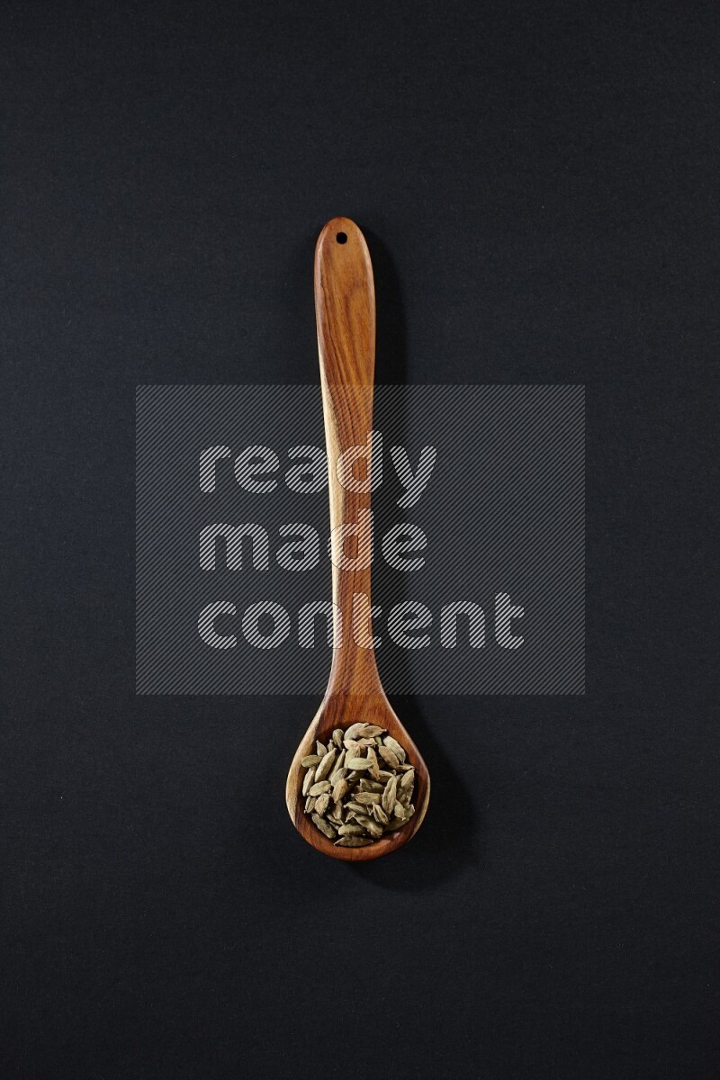 A wooden ladle full of cardamom on black flooring