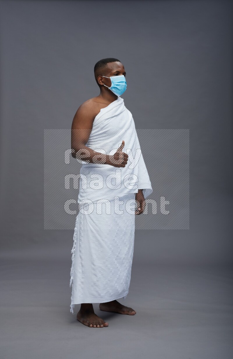 A man wearing Ehram with face mask Standing Interacting with the camera on gray background
