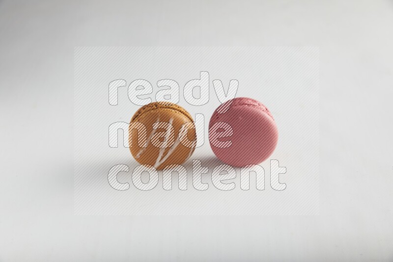 45º Shot of of two assorted Brown Irish Cream, and Pink Raspberry macarons on white background