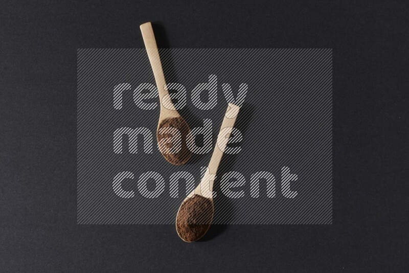 2 wooden spoons full of cloves powder on a black flooring