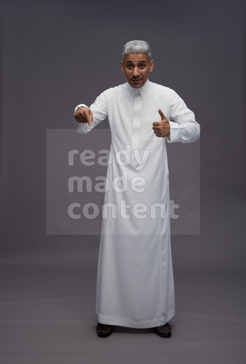 Saudi man wearing thob standing interacting with the camera on gray background
