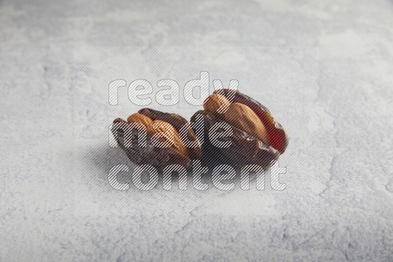 two almond stuffed madjoul dates on a light grey background